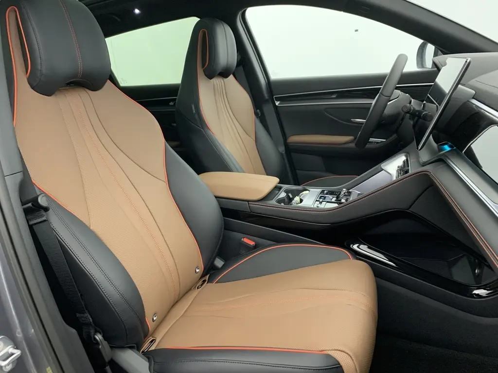 Vue intérieure côté conducteur du BYD SEAL U 2025, sièges en similicuir noir et marron avec surpiqûres orange et accoudoir central beige.