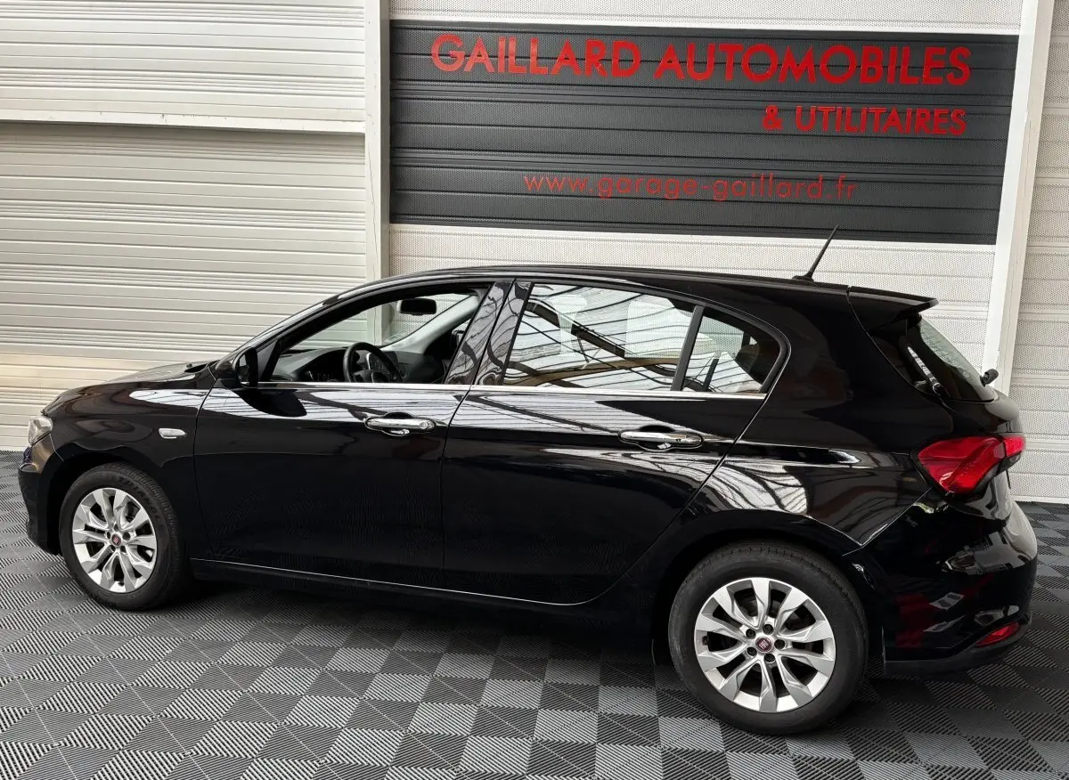 Profil gauche d'une FIAT TIPO noire de 2017, compacte avec jantes alliage et vitres teintées, en intérieur showroom.