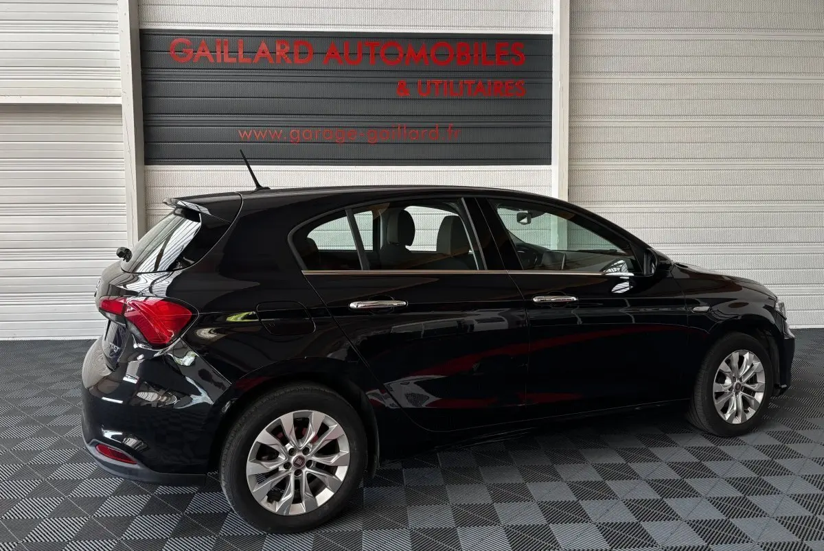 Vue latérale droite d'une FIAT Tipo noire 5 portes garée en intérieur avec jantes alliage et feux arrière visibles.