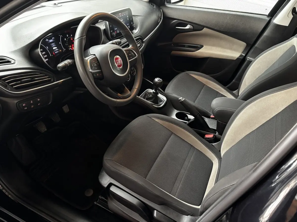 Intérieur avant droit de la Fiat Tipo 2017, volant cuir alu multifonctions et sièges tissu noir avec surpiqûres grises.