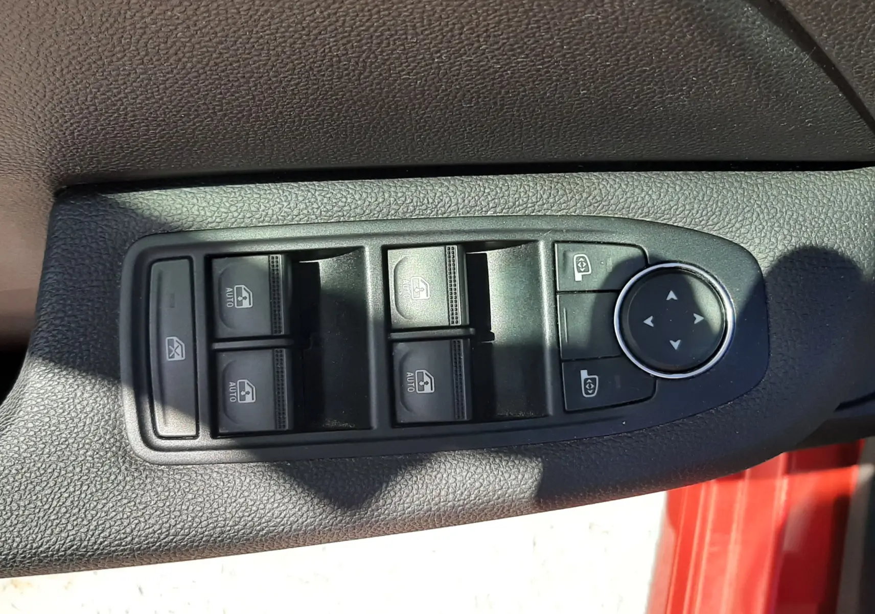 Gros plan sur les commandes des vitres électriques et rétroviseurs sur la porte côté conducteur d'une Renault Clio V rouge.