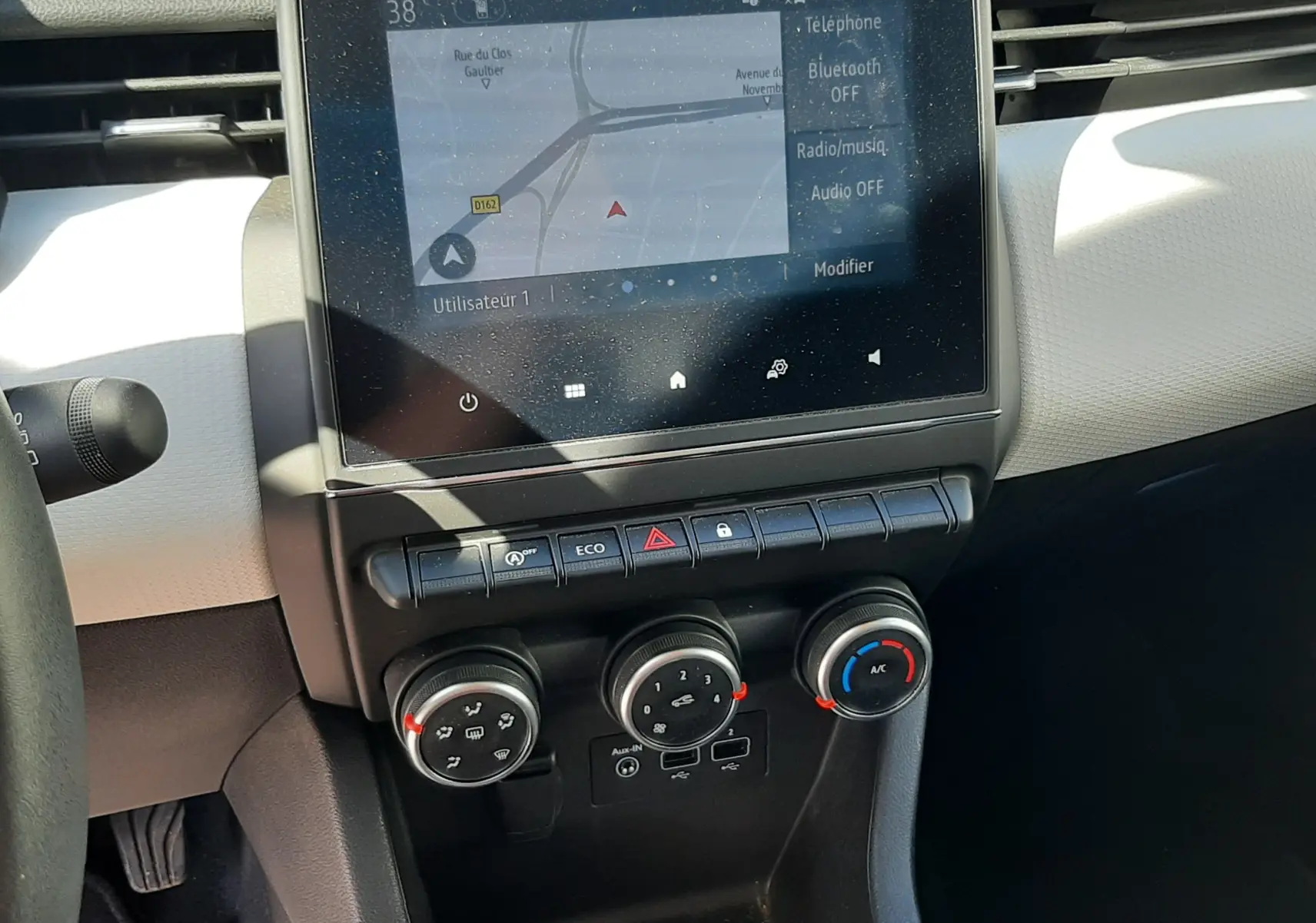 Vue rapprochée de la console centrale de la Renault Clio V rouge, avec écran tactile et commandes de climatisation.