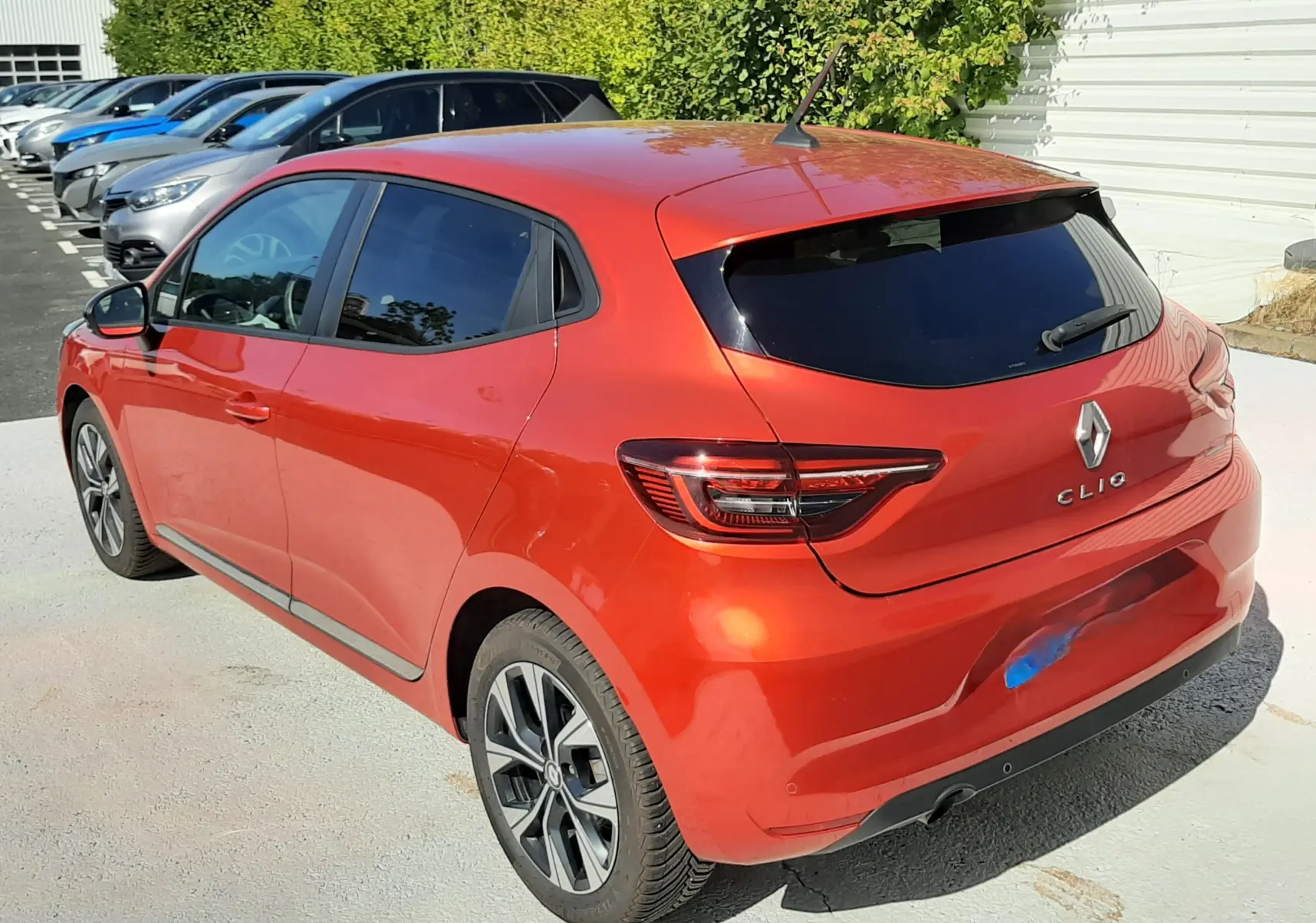 Vue 3/4 arrière droite d'une Renault Clio V rouge 5 portes, avec vitres teintées et jantes alliage bicolores.