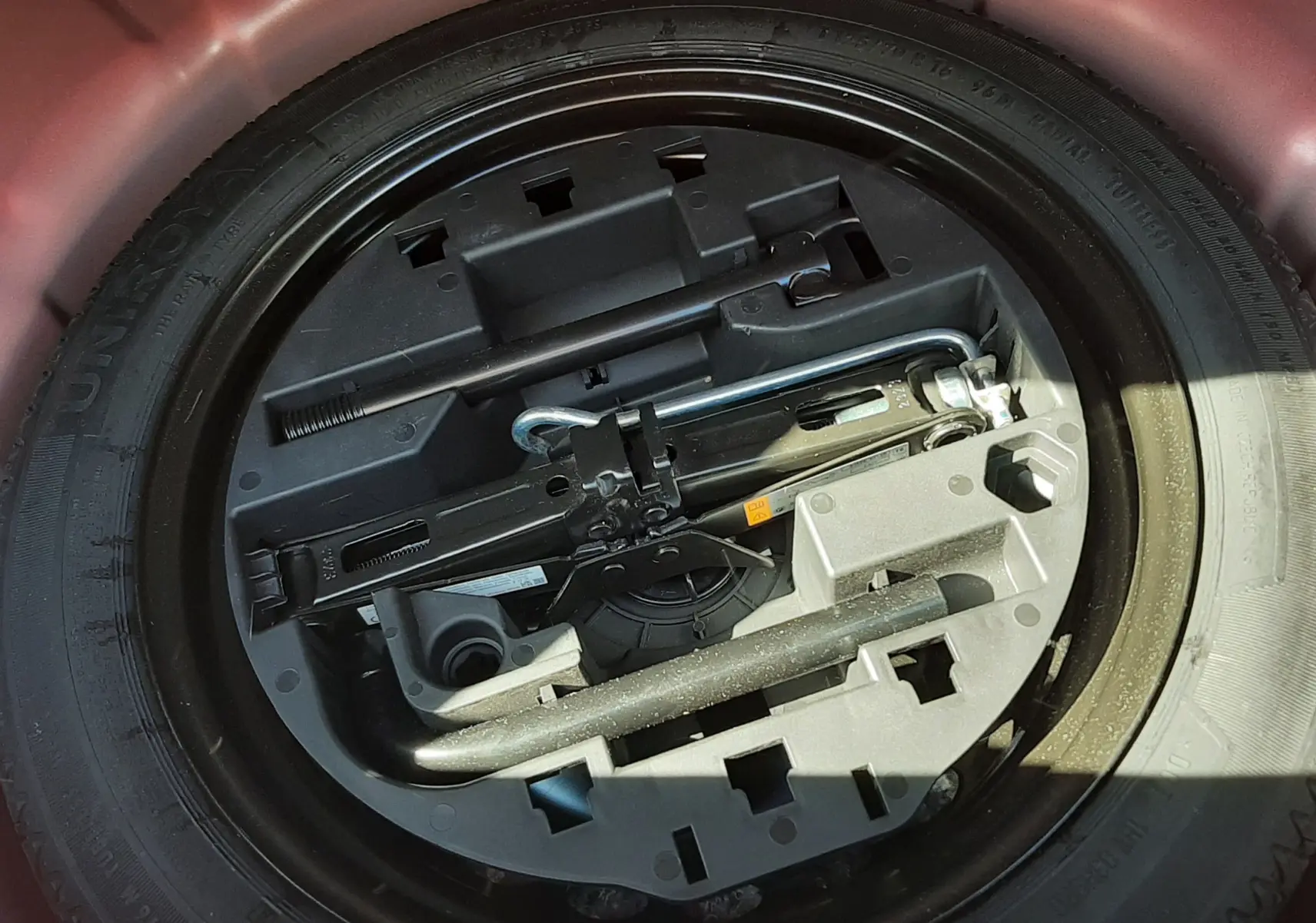 Roue de secours et kit d'outils rangés dans le coffre d'une Renault Clio V rouge, vue en plongée.