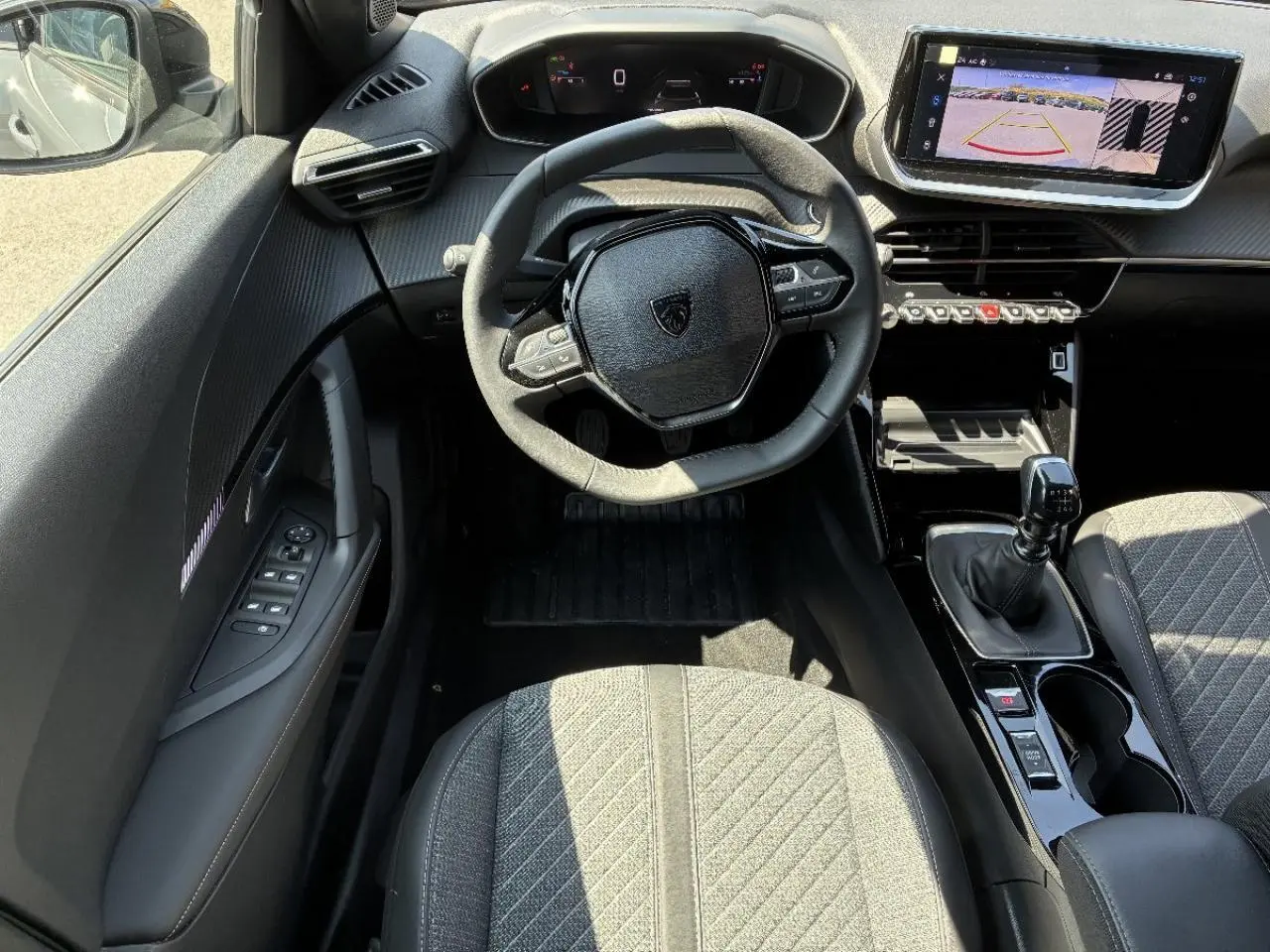 Vue intérieure centrée sur le volant et la console centrale d'une Peugeot 2008 2024 essence, sellerium, boîte manuelle.