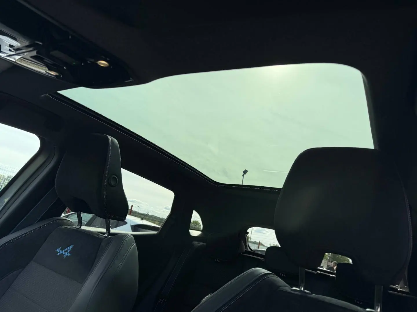 Vue intérieure du Renault Austral 2026, toit panoramique, sièges avant noirs avec logo Alpine bleu brodé.