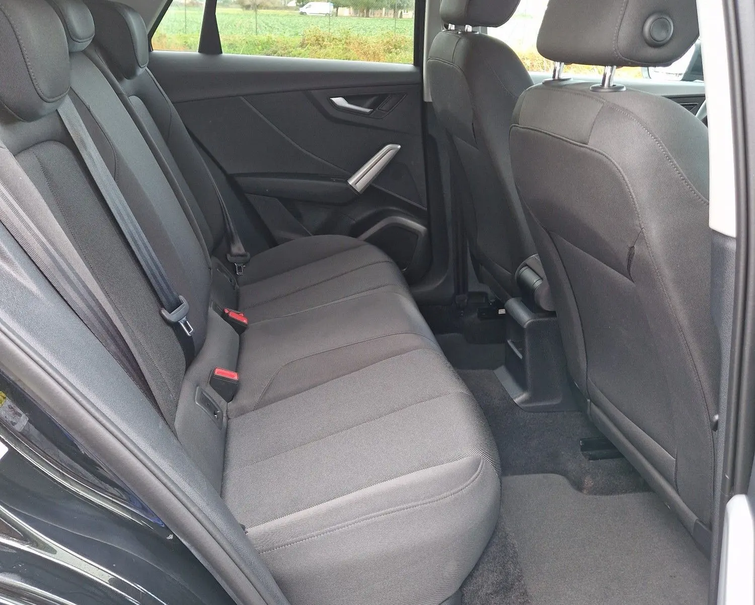 Vue intérieure arrière côté droit de l'Audi Q2 35 TFSI 2023 noir mito metal, sièges tissu noir et ceintures visibles.