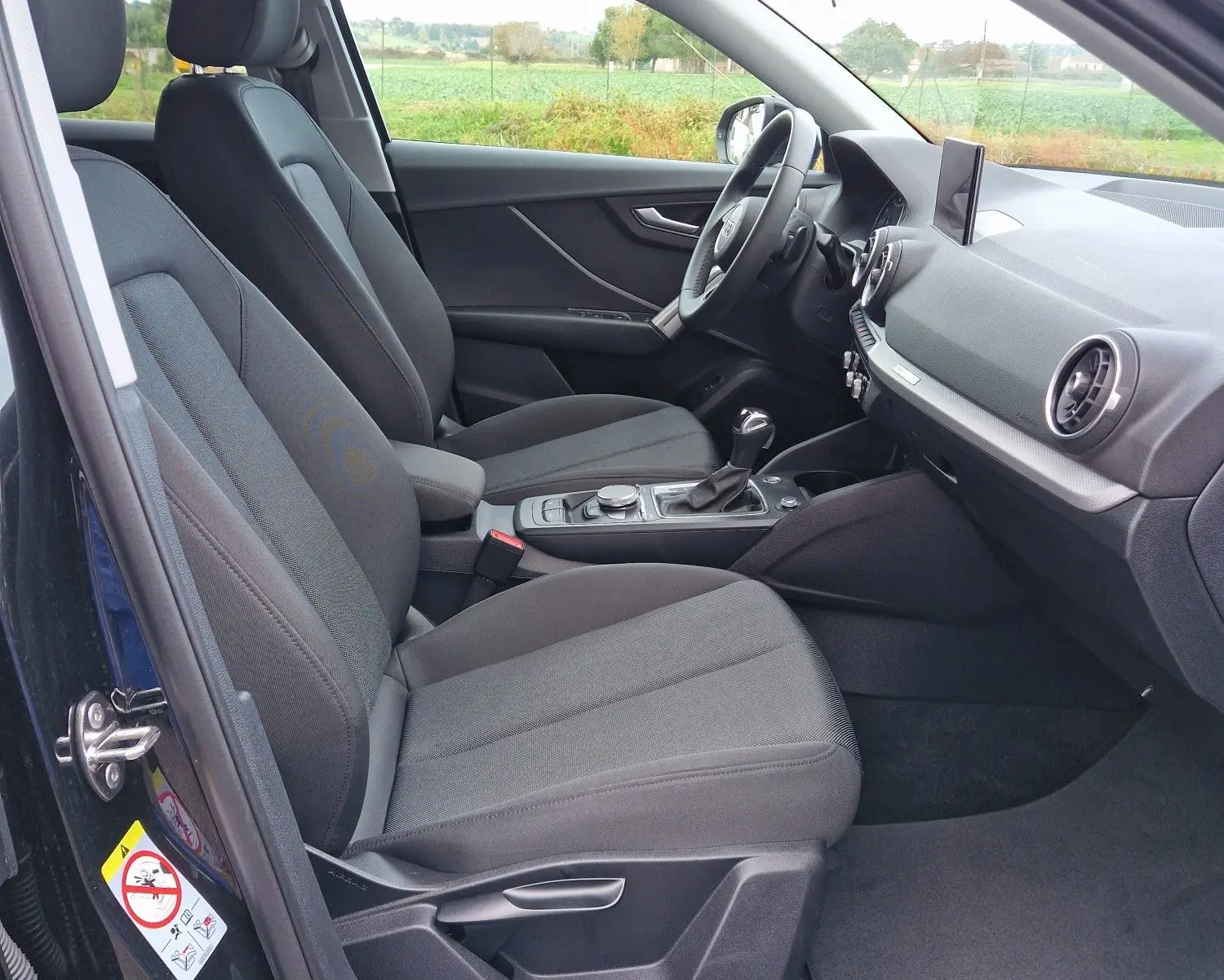 Intérieur côté conducteur de l'Audi Q2 noir mito metal 2023, montrant sièges tissu noir et tableau de bord moderne.
