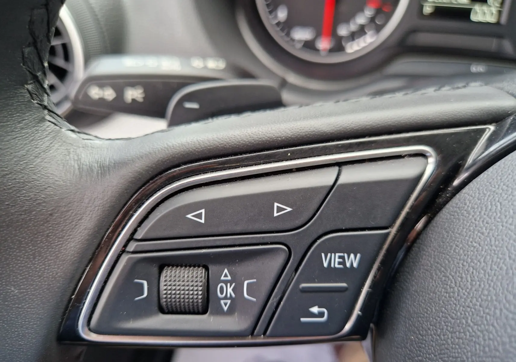 Gros plan sur les commandes multifonctions du volant noir de l'Audi Q2 35 TFSI 2023, boutons directionnels et "VIEW" visibles.