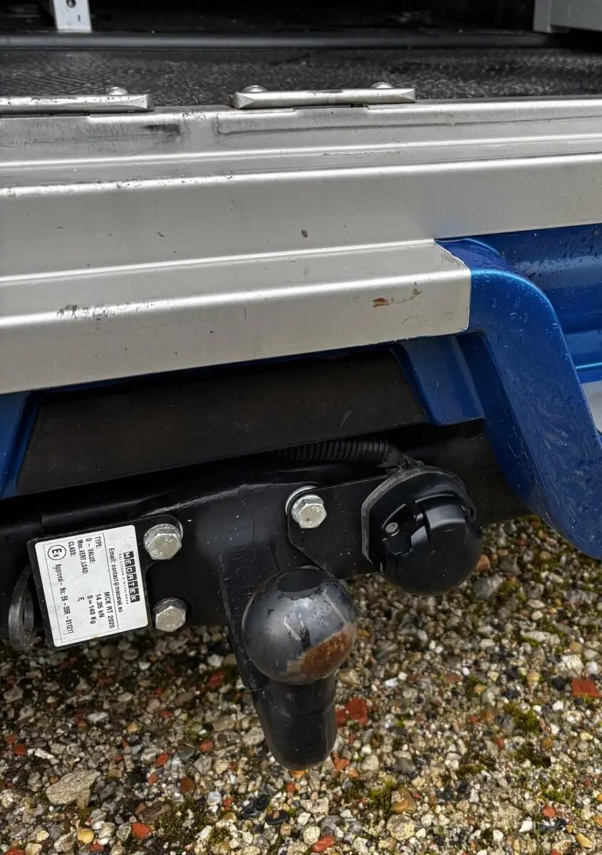 Gros plan sur l'attelage arrière noir rouillé d'un Renault Master bleu, avec partie inférieure de la benne en métal gris.