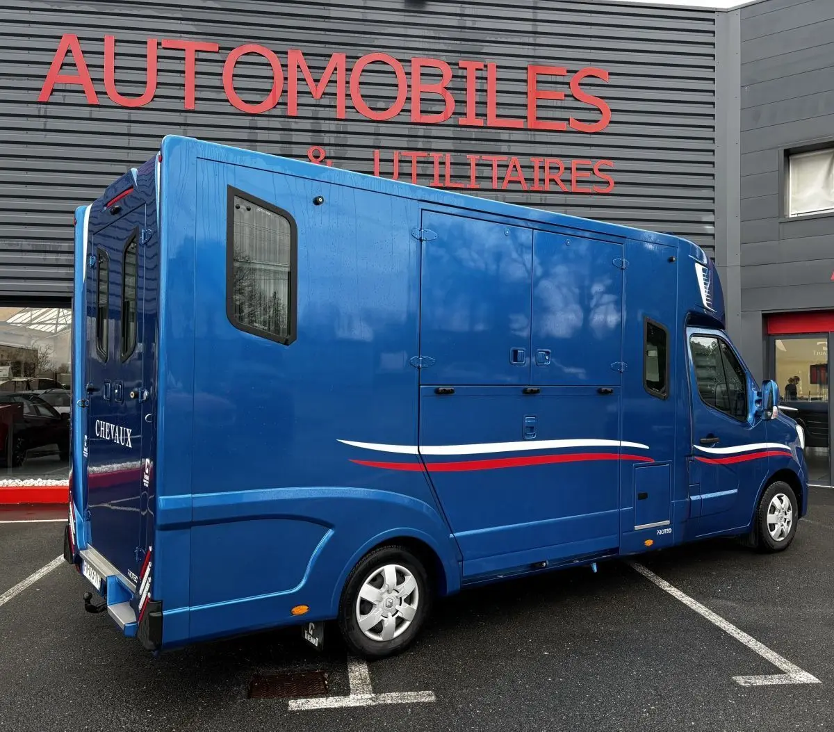 Vue 3/4 arrière droite d’un Renault Master bleu avec marquage tricolore et aménagement chevaux visible sur la porte arrière.