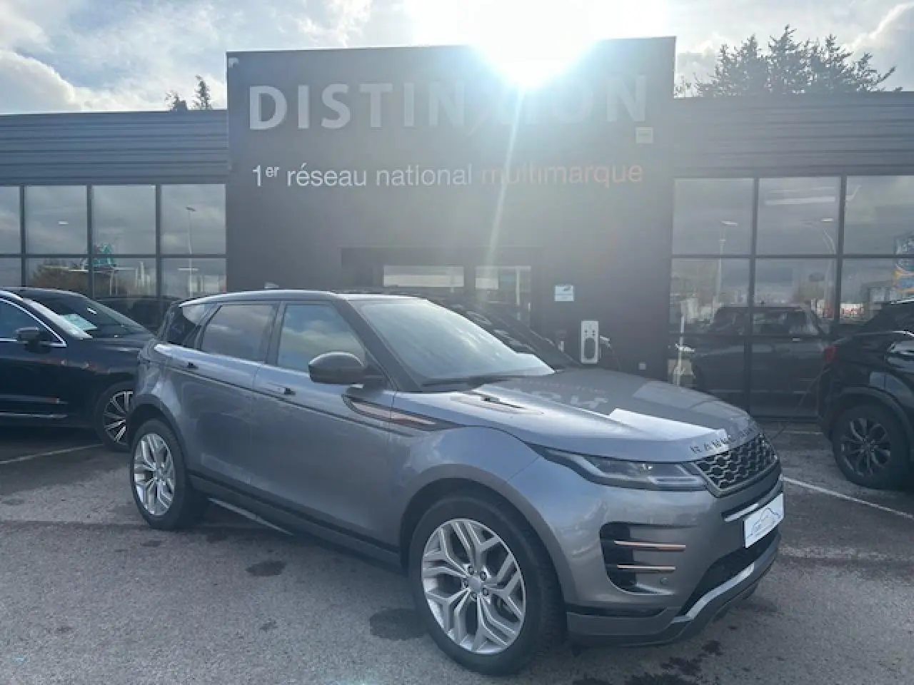 Vue 3/4 avant droit d'un Range Rover Evoque gris foncé avec toit noir et jantes 20 pouces, stationné devant un bâtiment.