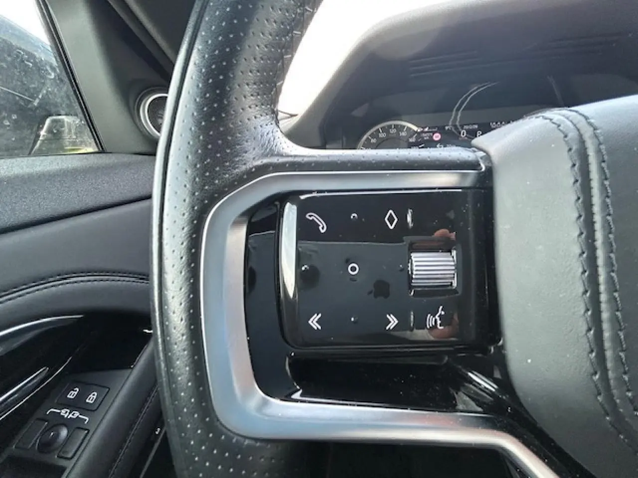 Gros plan sur le volant cuir perforé côté gauche du Range Rover Evoque gris foncé avec commandes intégrées et tableau de bord en arrière-plan.