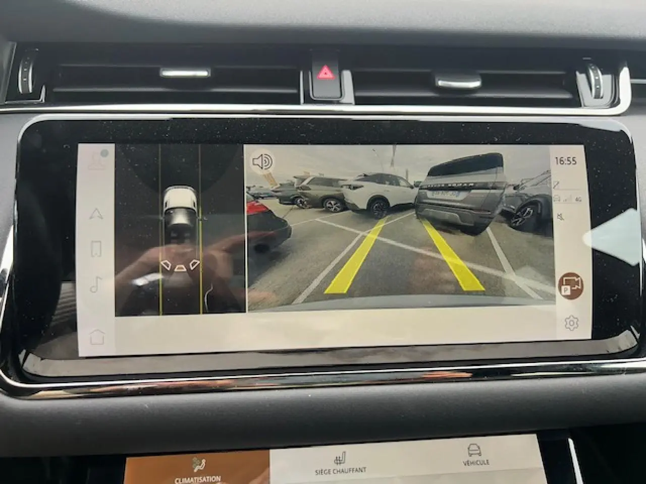 Écran tactile intérieur montrant la caméra de recul avec vue arrière sur un parking et plusieurs véhicules gris et blancs.