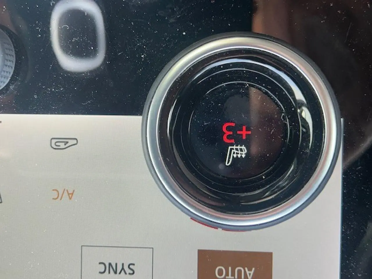 Gros plan sur le bouton de réglage de la température du siège chauffant dans le tableau de bord du Range Rover Evoque gris foncé.