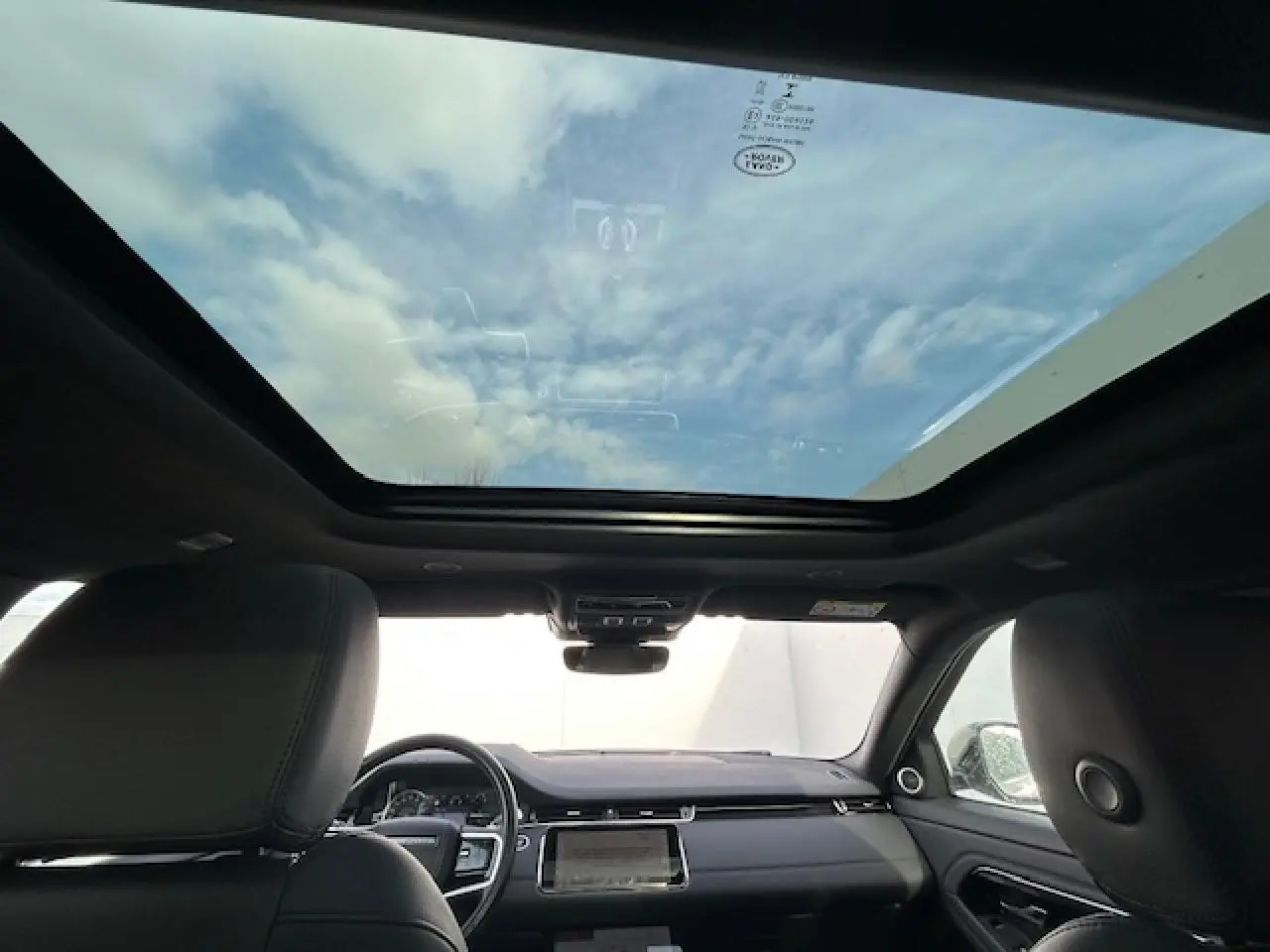 Vue intérieure avant du Range Rover Evoque gris foncé 2022 avec toit ouvrant panoramique et tableau de bord moderne.
