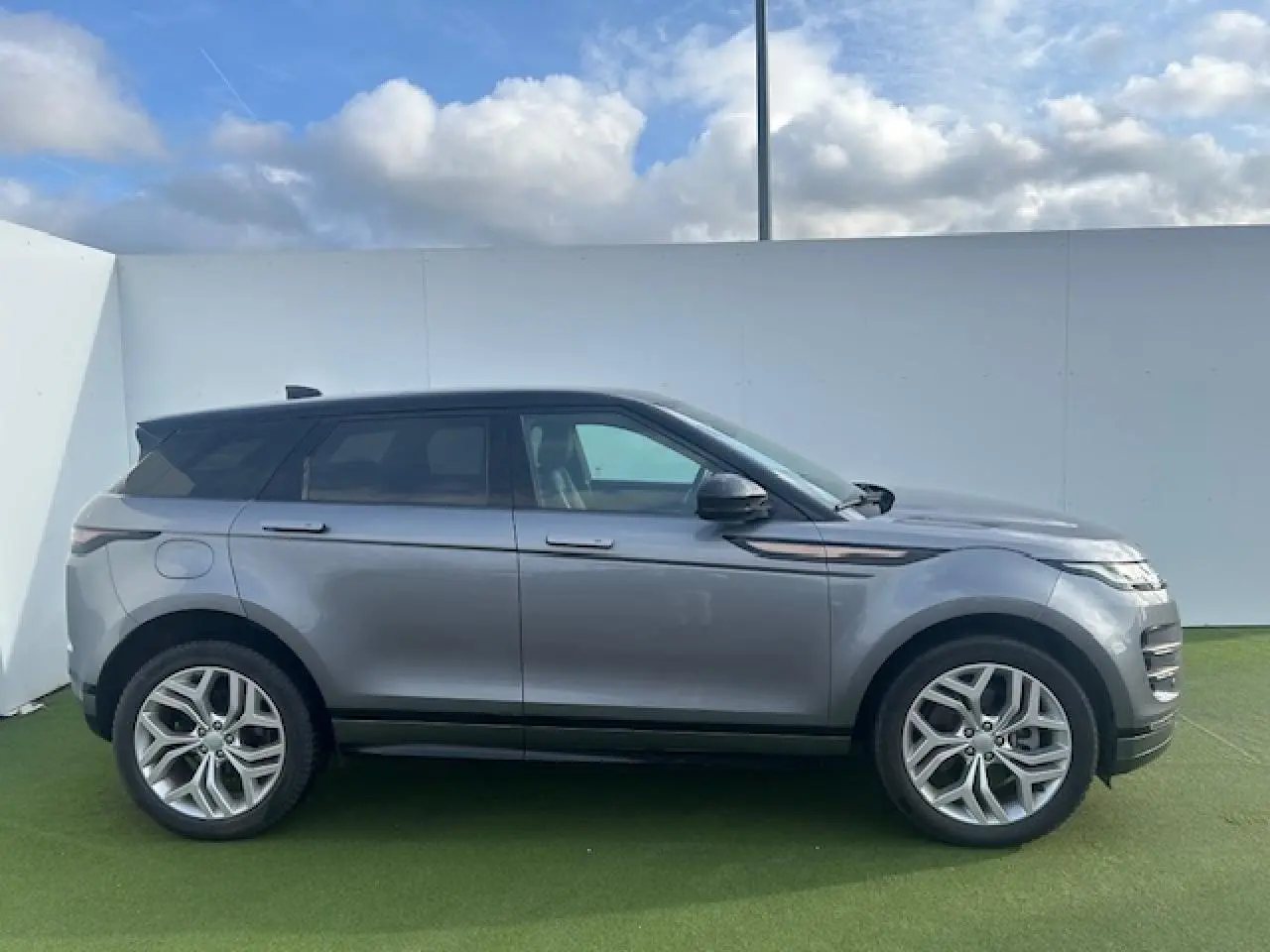 Vue latérale droite d'un Range Rover Evoque gris foncé avec toit noir et jantes 20 pouces sur fond extérieur clair.