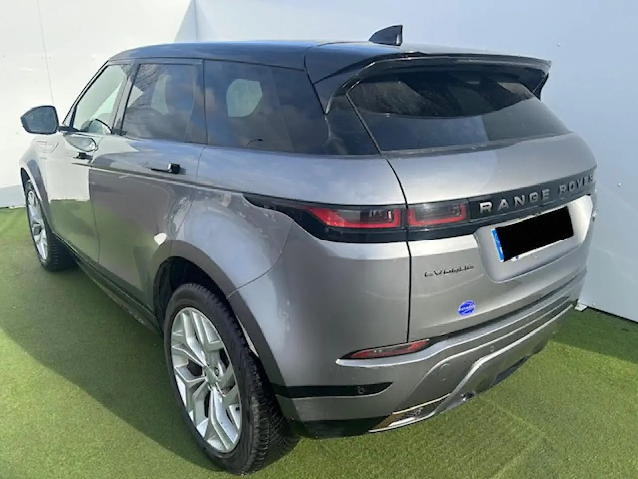 Vue 3/4 arrière droite d'un Range Rover Evoque gris foncé avec toit noir et jantes 20 pouces sur sol vert.