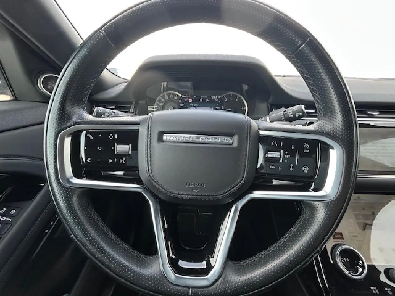 Volant cuir noir avec commandes intégrées et logo Range Rover, tableau de bord et écran tactile partiel visibles.