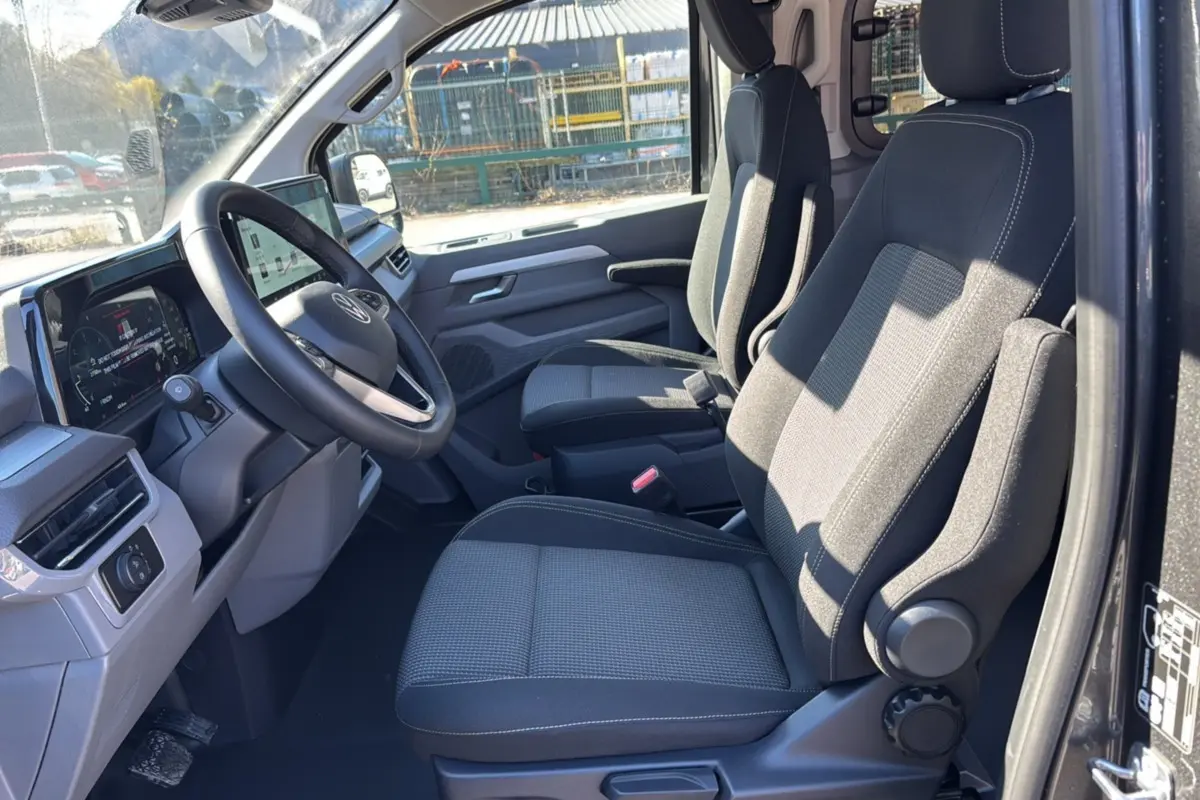 Vue intérieure côté conducteur du Volkswagen Transporter TDI 170 DSG ProCab 2026 avec sièges tissu gris et tableau de bord digital.
