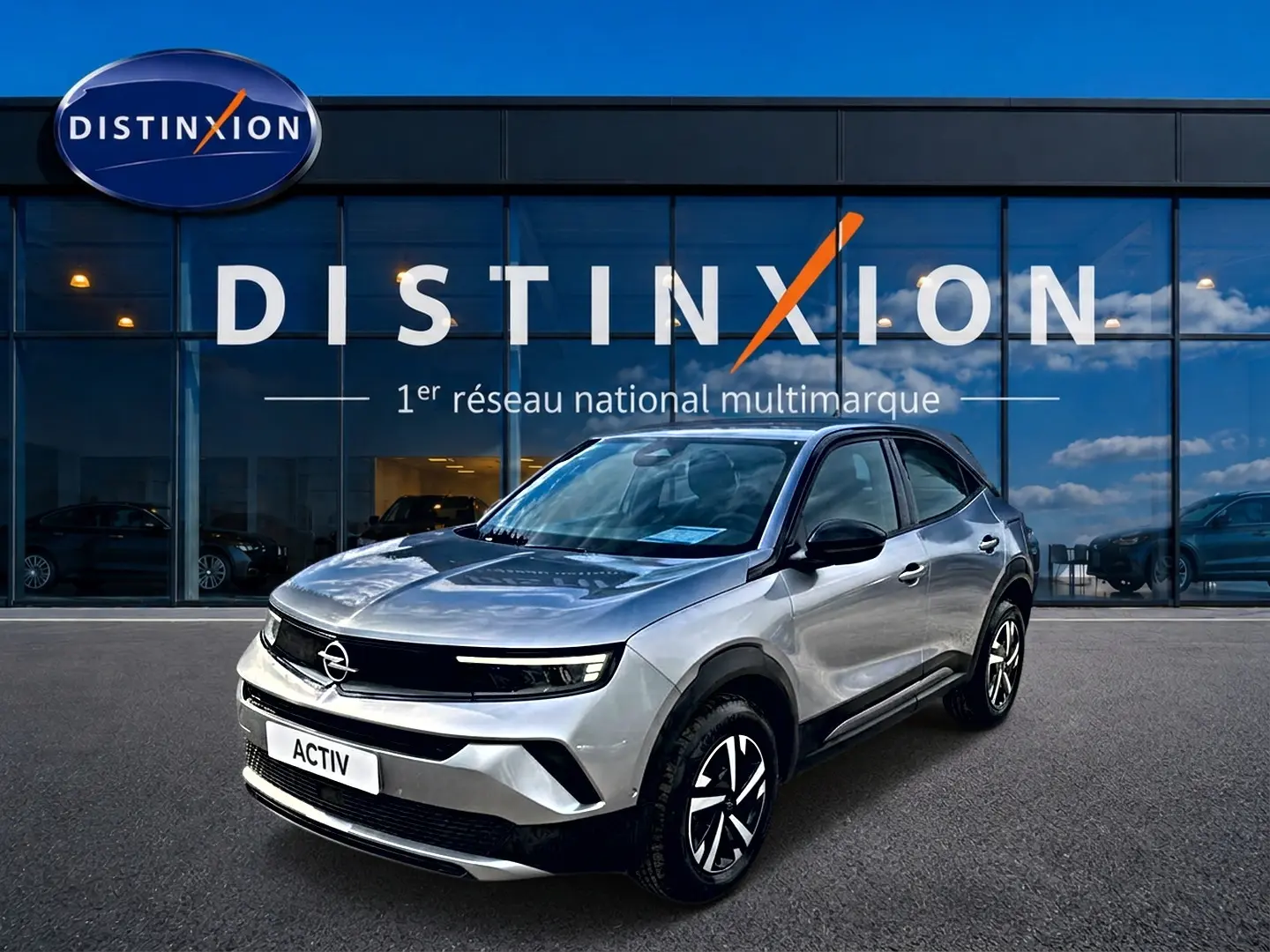 Opel Mokka gris en 3/4 avant droit, avec jantes noires et calandre noire brillante devant showroom Distinxion.