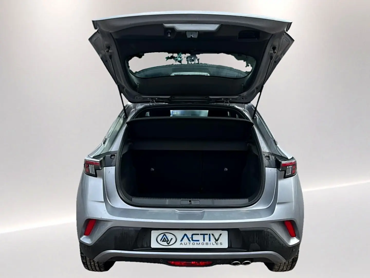 Vue arrière d’un Opel Mokka gris 2025 avec le coffre ouvert, feux arrière LED et double sortie d’échappement visible.
