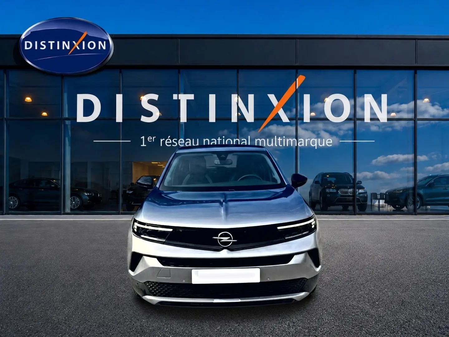 Opel Mokka gris 2025 vue de face, avec calandre noire et logo Opel centré devant un showroom Distinxion.