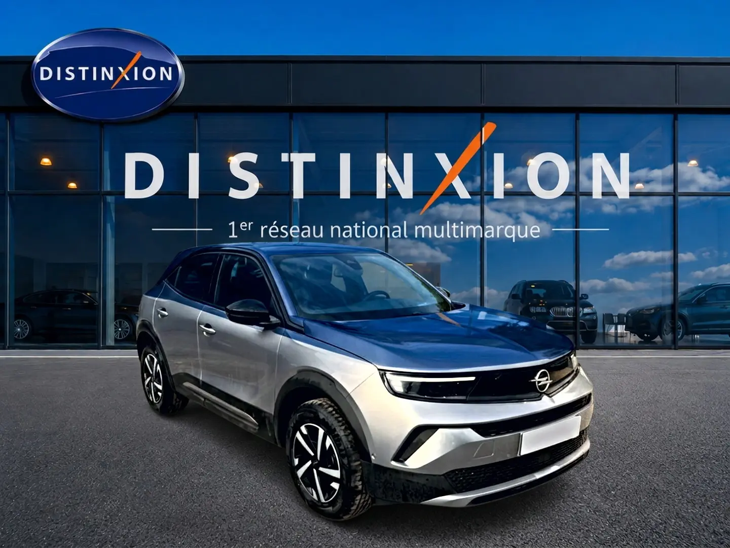 Opel Mokka gris 3/4 avant droit, avec jantes noires et toit noir, devant vitrine Distinxion.