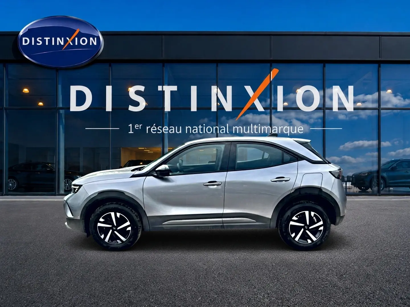 Opel Mokka gris vue de profil côté gauche, avec jantes noires et toit contrasté blanc devant showroom Distinxion.