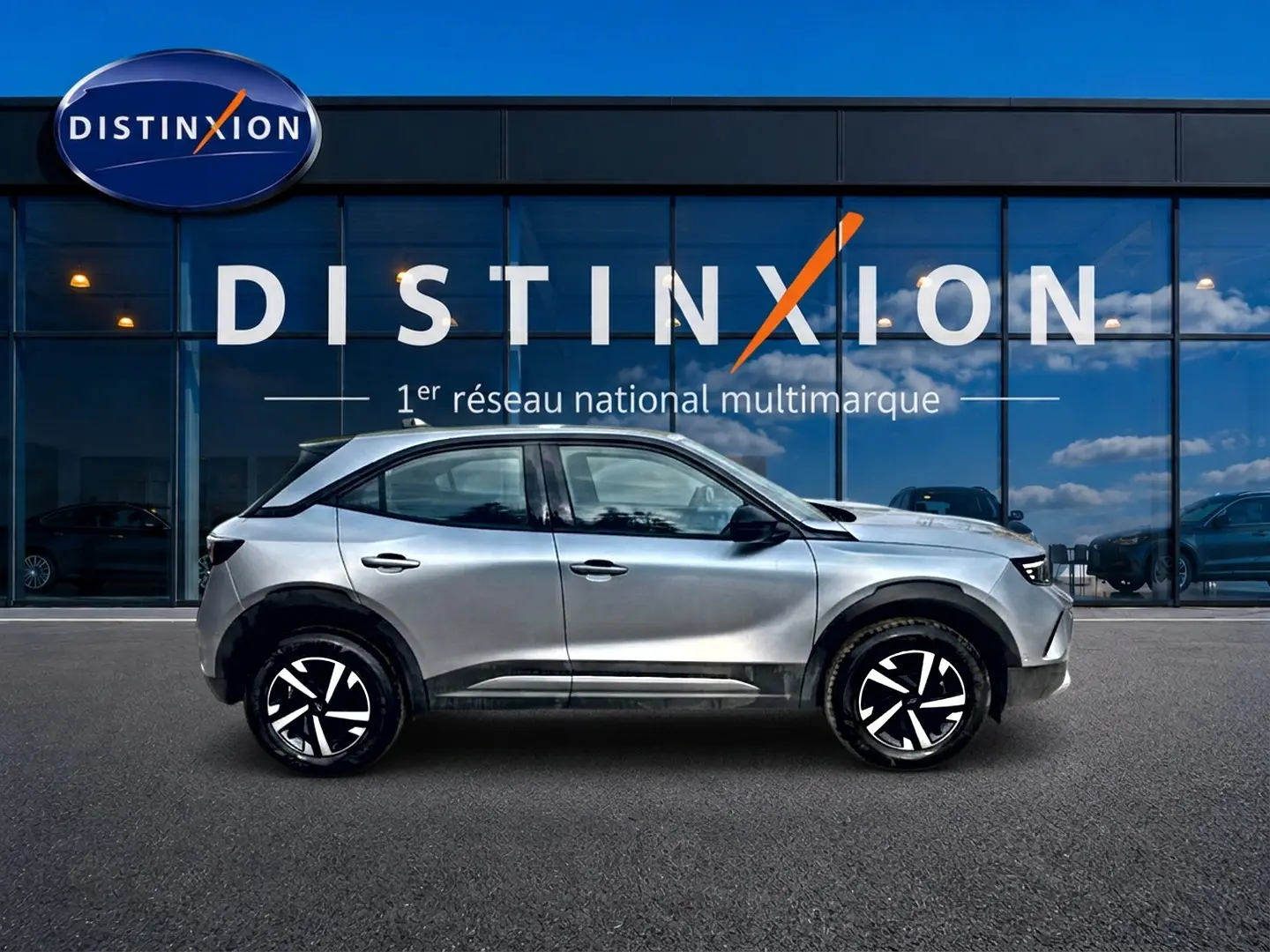 Opel Mokka gris vue de profil côté gauche, avec jantes noires et blanches, devant une vitrine Distinxion.