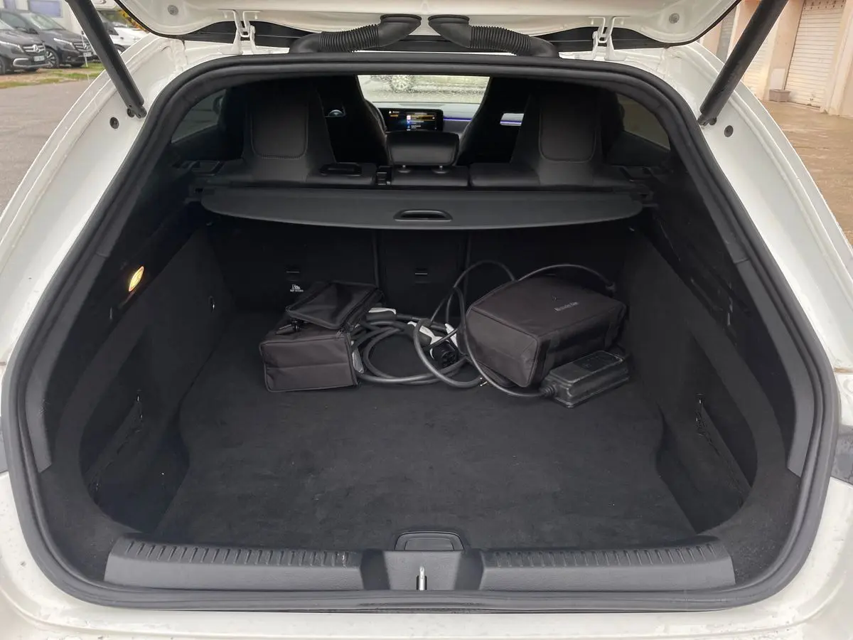 Coffre ouvert d'une Mercedes CLA Shooting Brake blanche, vue arrière montrant l'espace de chargement et câbles de recharge hybride.