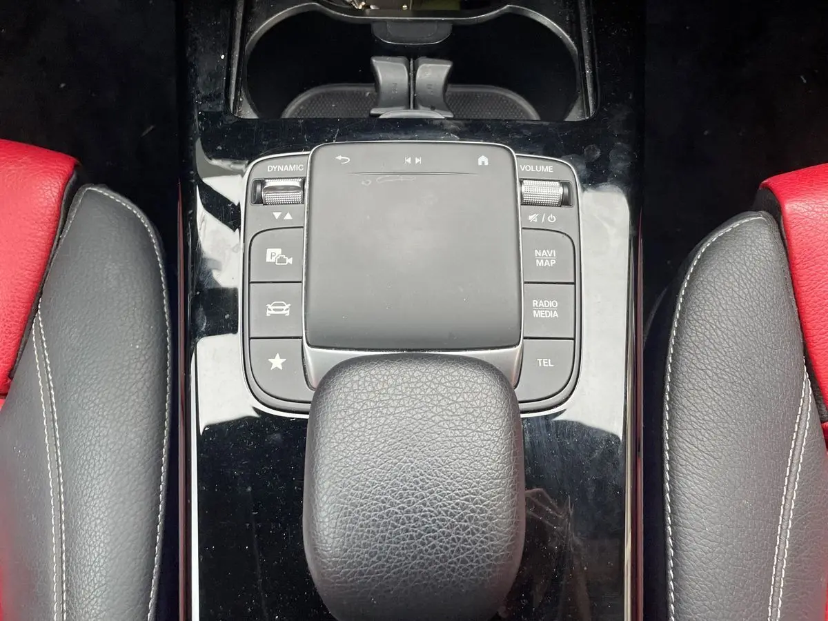 Gros plan sur la console centrale noire avec pavé tactile et pommeau de boîte automatique, sièges cuir rouge et noir visibles.