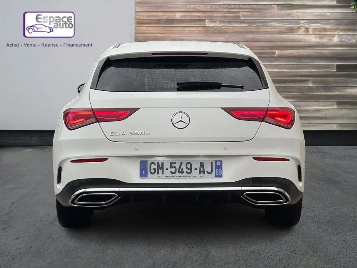Vue arrière d'une Mercedes CLA Shooting Brake blanche avec feux allumés et double sortie d'échappement chromée.