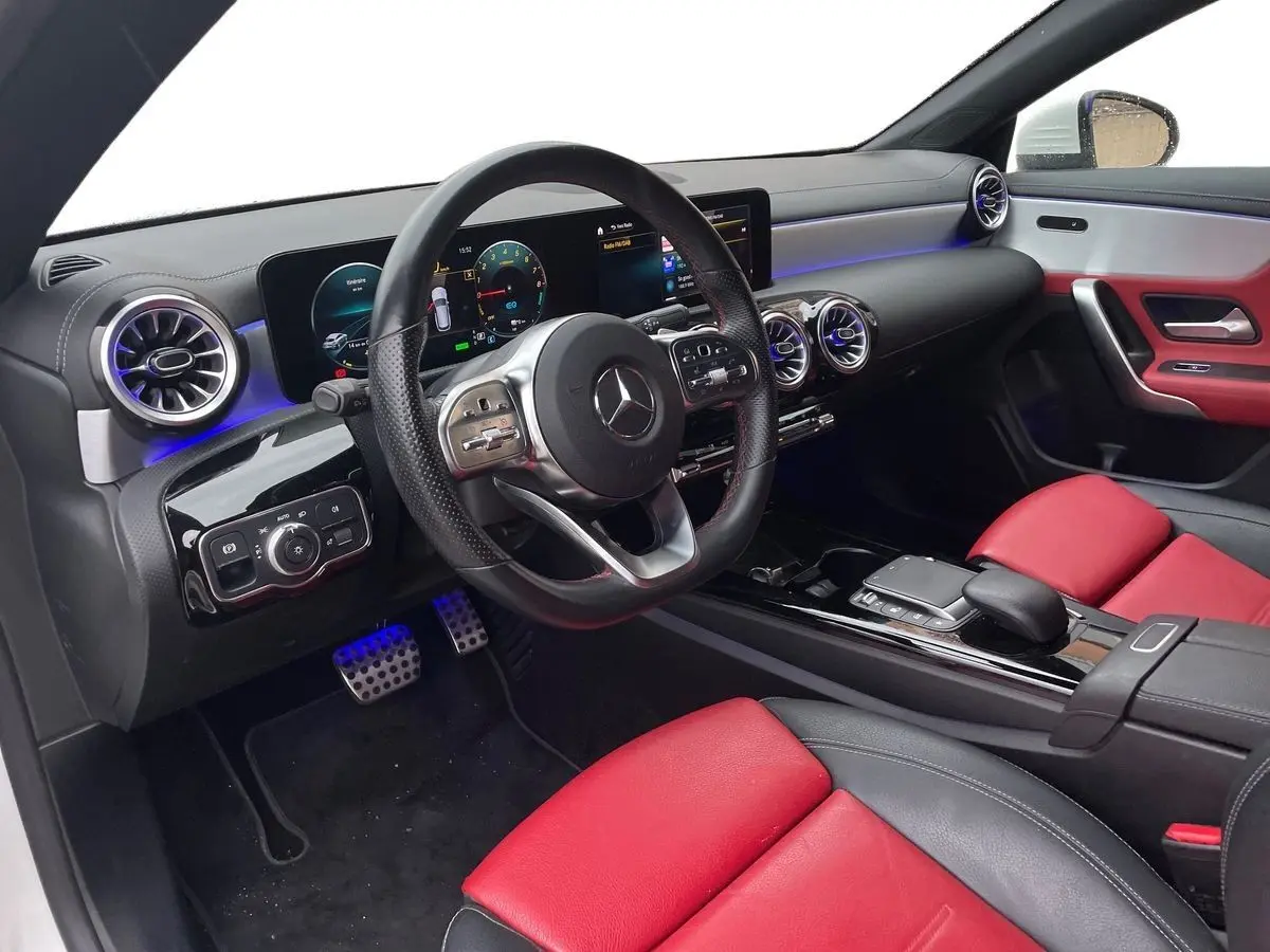 Intérieur côté conducteur de la Mercedes CLA Shooting Brake blanc, sièges cuir rouge et noir, tableau de bord digital AMG Line.
