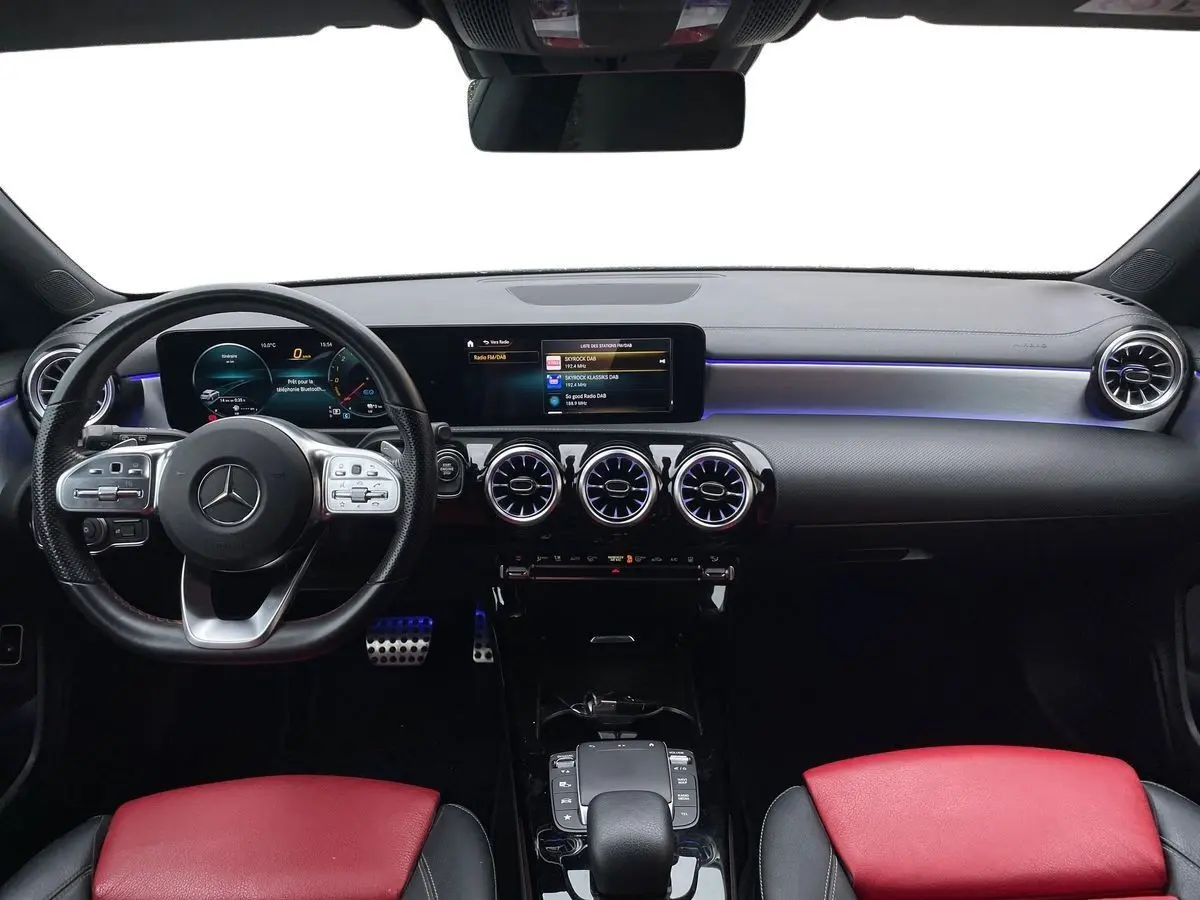 Intérieur de Mercedes Classe CLA Shooting Brake blanc 2021, vue frontale du tableau de bord avec sièges rouges et éclairage bleu.