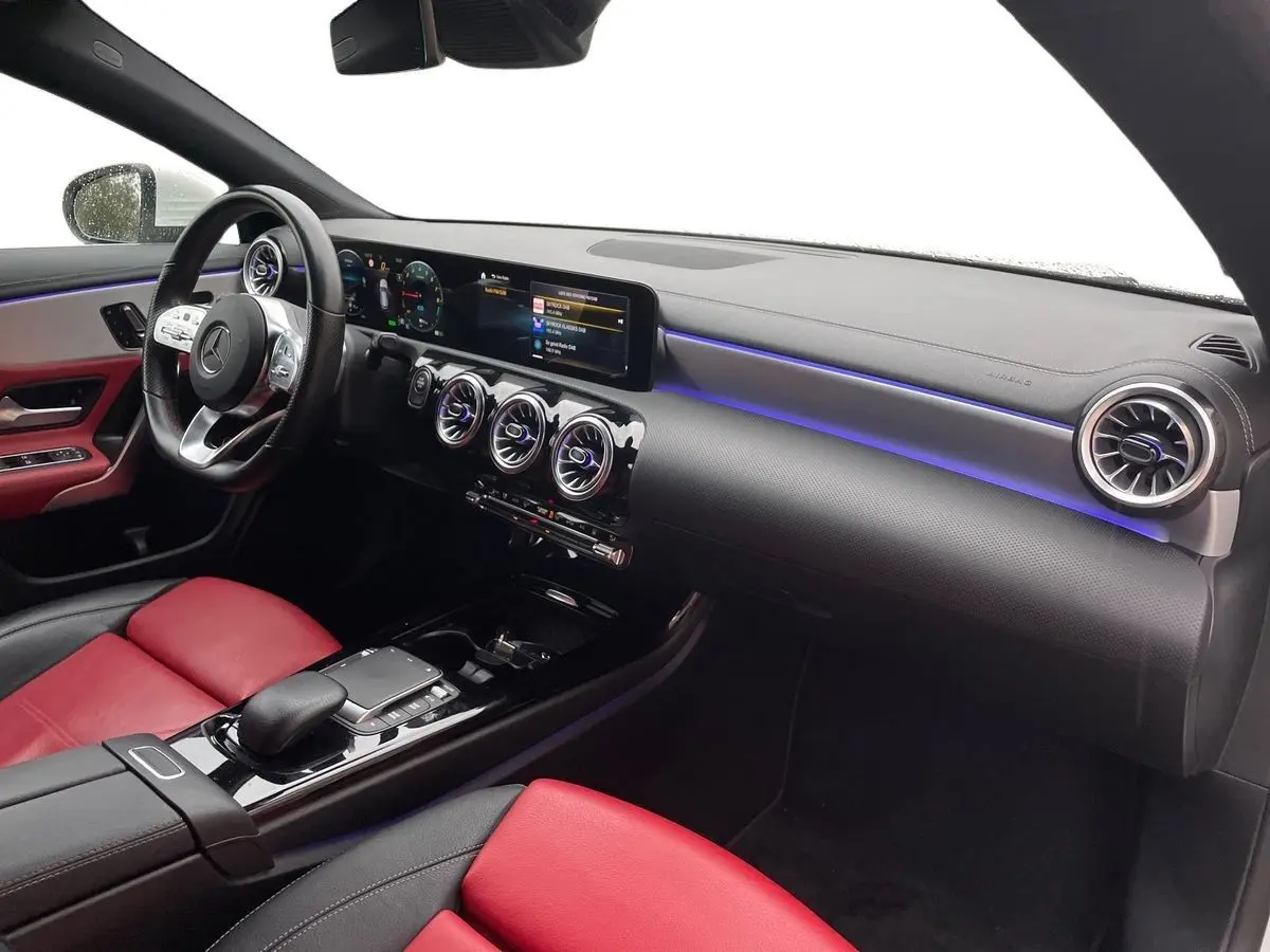 Vue intérieure côté passager de la Mercedes CLA Shooting Brake 250 E AMG Line 2021 avec sièges cuir rouge et éclairage d'ambiance bleu.