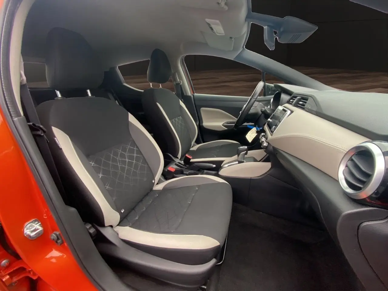 Vue intérieure côté gauche de la Nissan Micra orange Energy 2022, montrant les sièges tissu noir et beige et le tableau de bord clair.