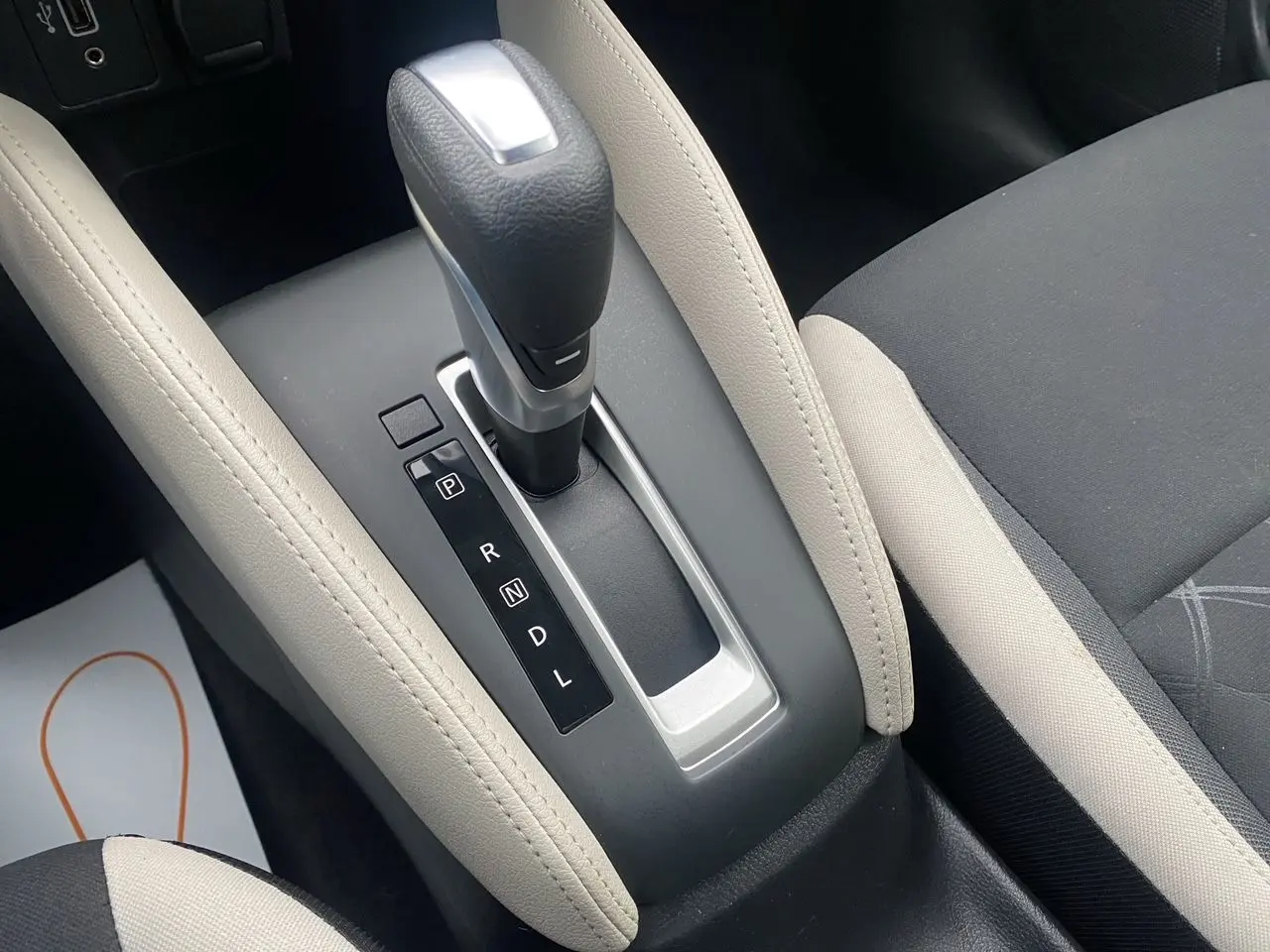 Le levier de vitesses automatique noir et argenté de la Nissan Micra 2022, entouré d’un accoudoir beige et siège tissu noir-beige.