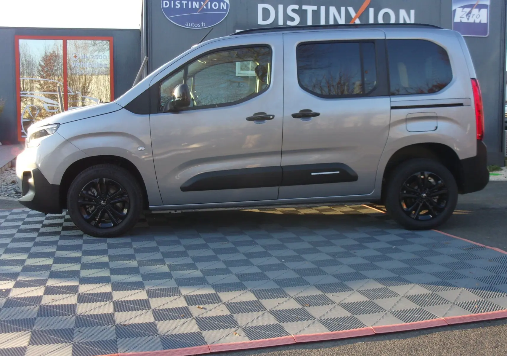 Vue de profil côté gauche d'un Citroën Berlingo gris Artense avec jantes noires et protections latérales noires.