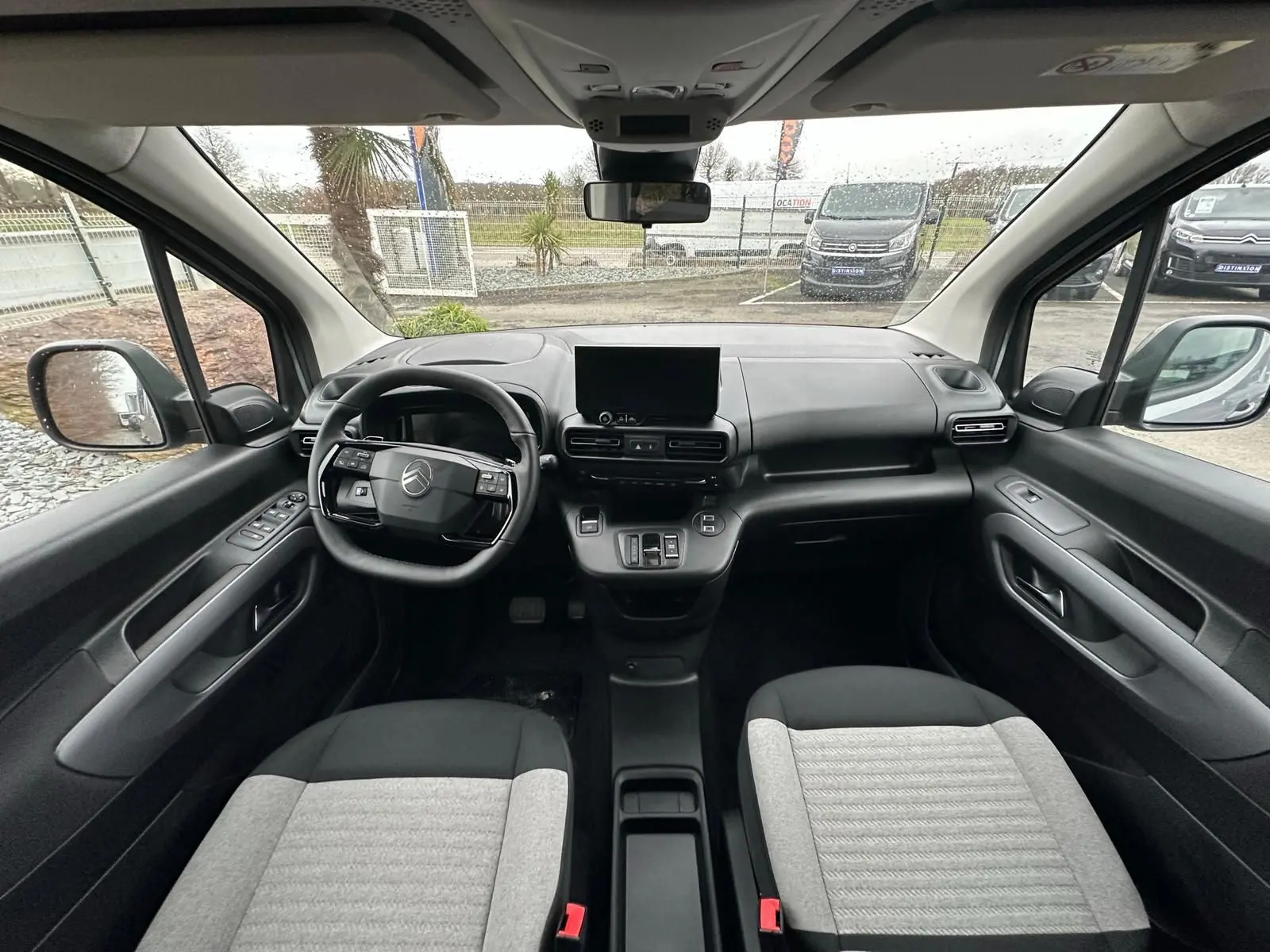 Vue intérieure avant du Citroën Berlingo 2025, montrant le tableau de bord noir et gris avec écran central et volant multifonction.