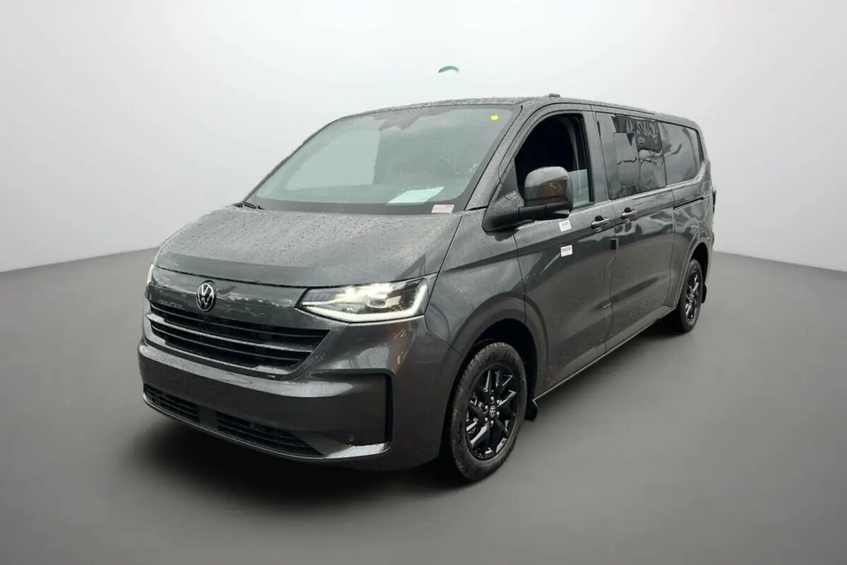 Vue 3/4 avant droite d’un Volkswagen Transporter TDI 170 DSG ProCab L2 gris graphite avec jantes alu noires et feux LED allumés.