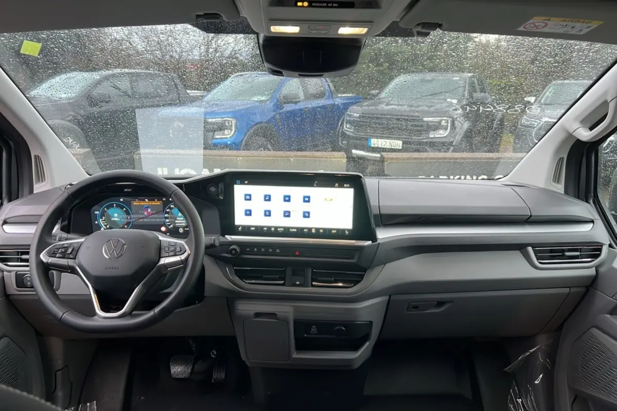Vue intérieure frontale du tableau de bord gris clair du Volkswagen Transporter TDI 170 DSG avec écran tactile et volant multifonctions.