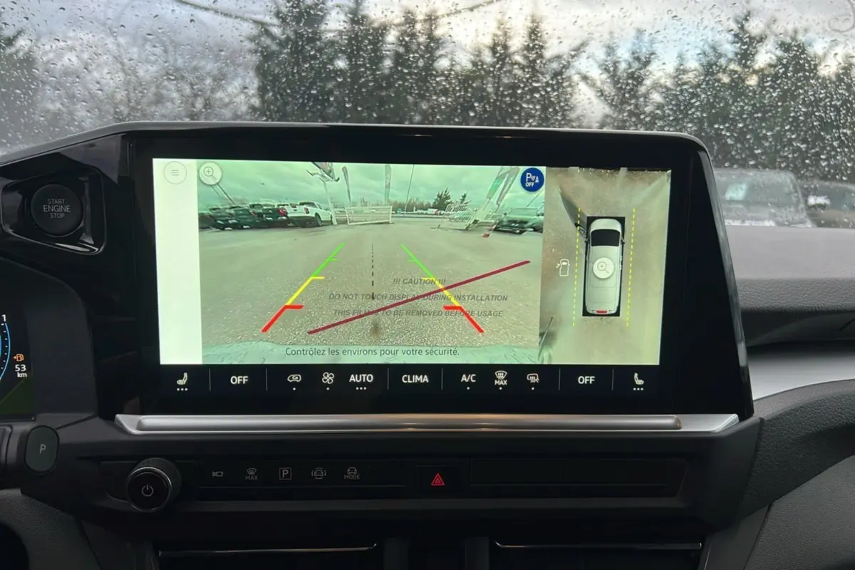 Vue intérieure du tableau de bord du Volkswagen Transporter TDI 170 DSG ProCab L2 avec écran de caméra 360 et pluie sur le pare-brise.