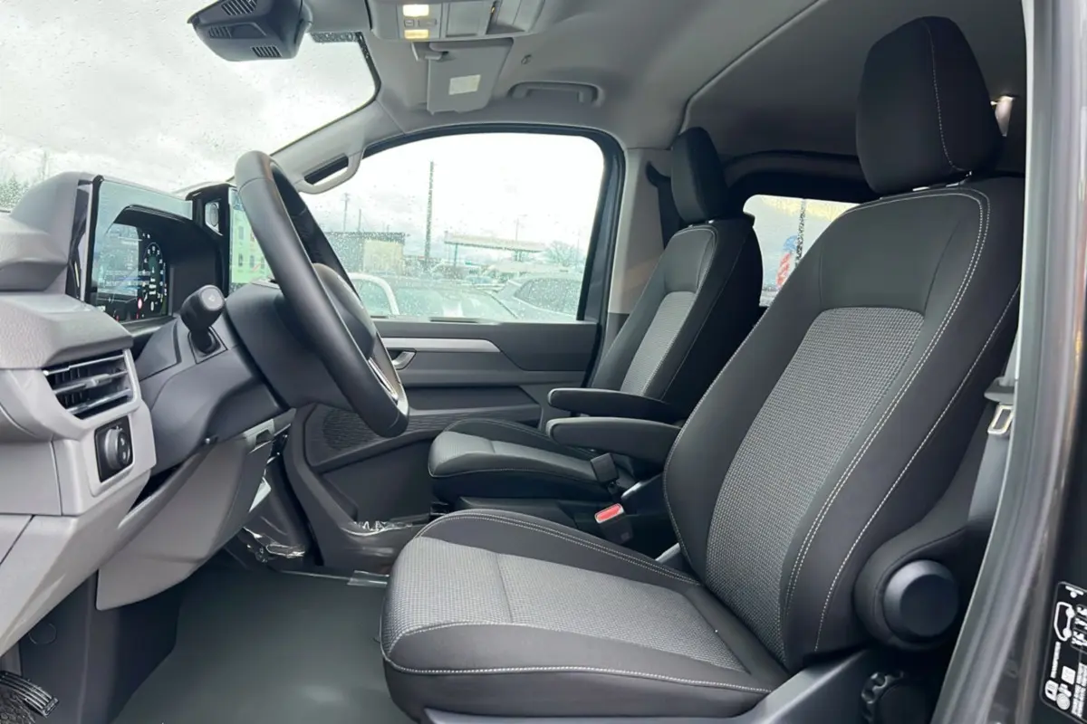 Vue intérieure côté conducteur du Volkswagen Transporter TDI 170 DSG Procab L2, sièges avant gris et noir avec accoudoirs.