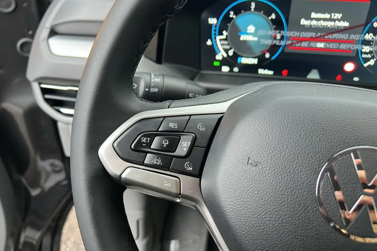 Gros plan sur le volant multifonctions noir du Volkswagen Transporter TDI 170 DSG 2026 avec tableau de bord digital en arrière-plan.