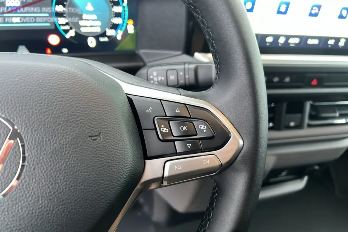 Gros plan sur le volant multifonctions noir du Volkswagen Transporter 2026 avec tableau de bord digital en arrière-plan.