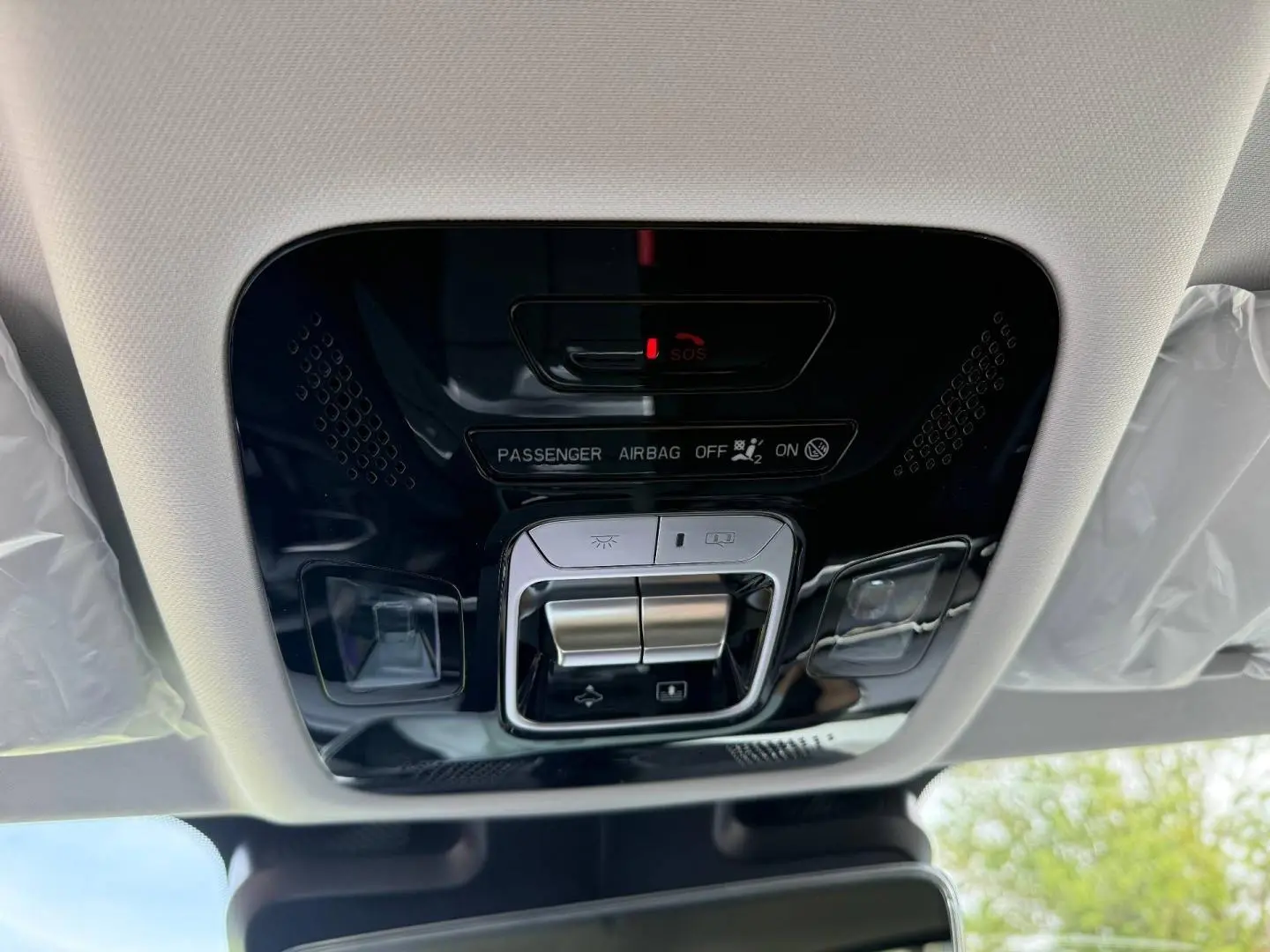 Vue intérieure en plongée sur la console de plafonnier noir brillant avec commandes d’éclairage et indicateur airbag passager du JAECOO J7 blanc.