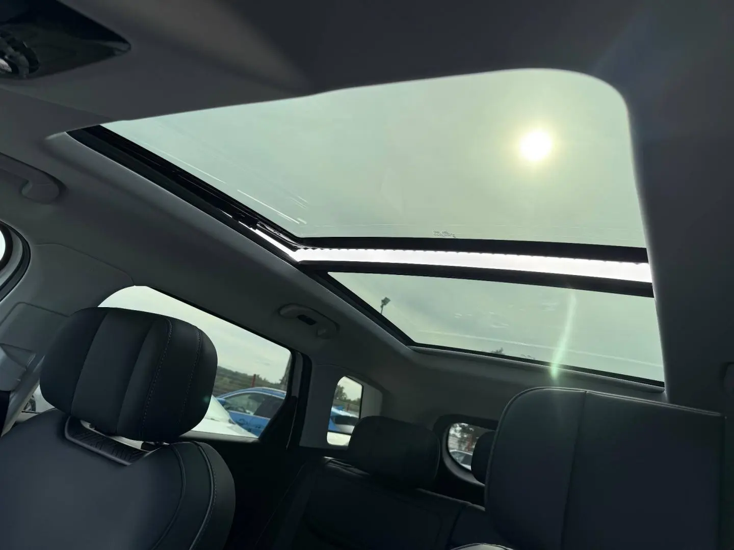 Vue intérieure du toit panoramique en verre du JAECOO J7 avec sièges avant en similicuir noir visibles.