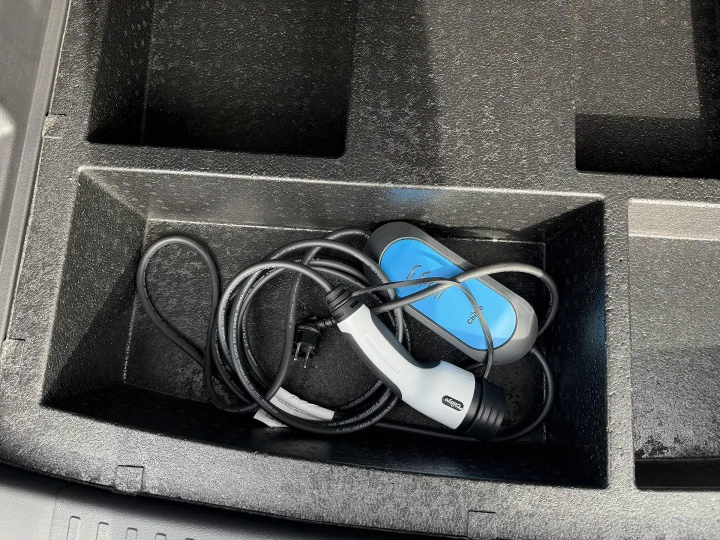Gros plan sur le câble de recharge bleu et blanc rangé dans le coffre du JAECOO J7 hybride rechargeable blanc.
