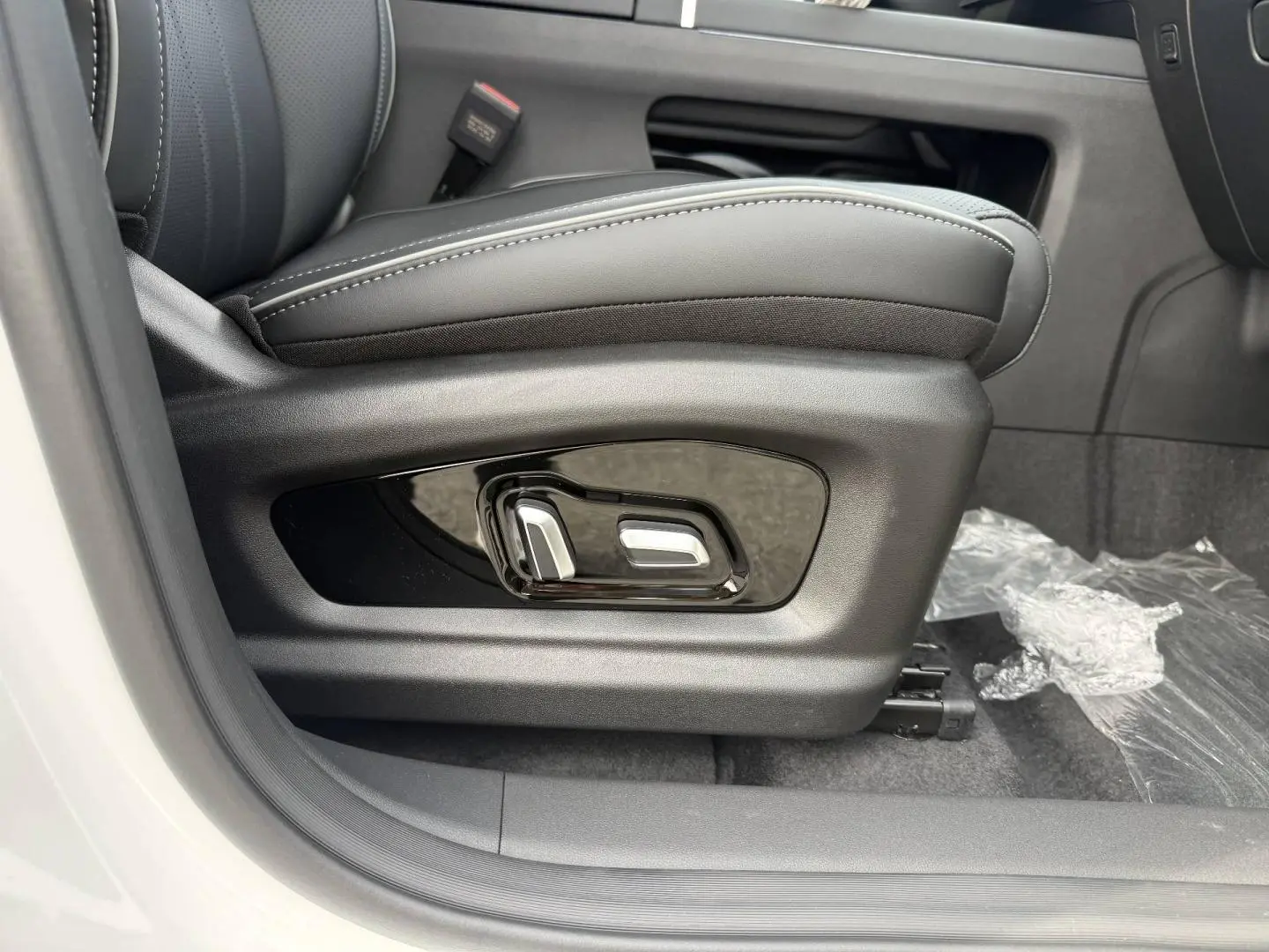 Gros plan sur les commandes électriques du siège conducteur noir dans un JAECOO J7 blanc, côté gauche.